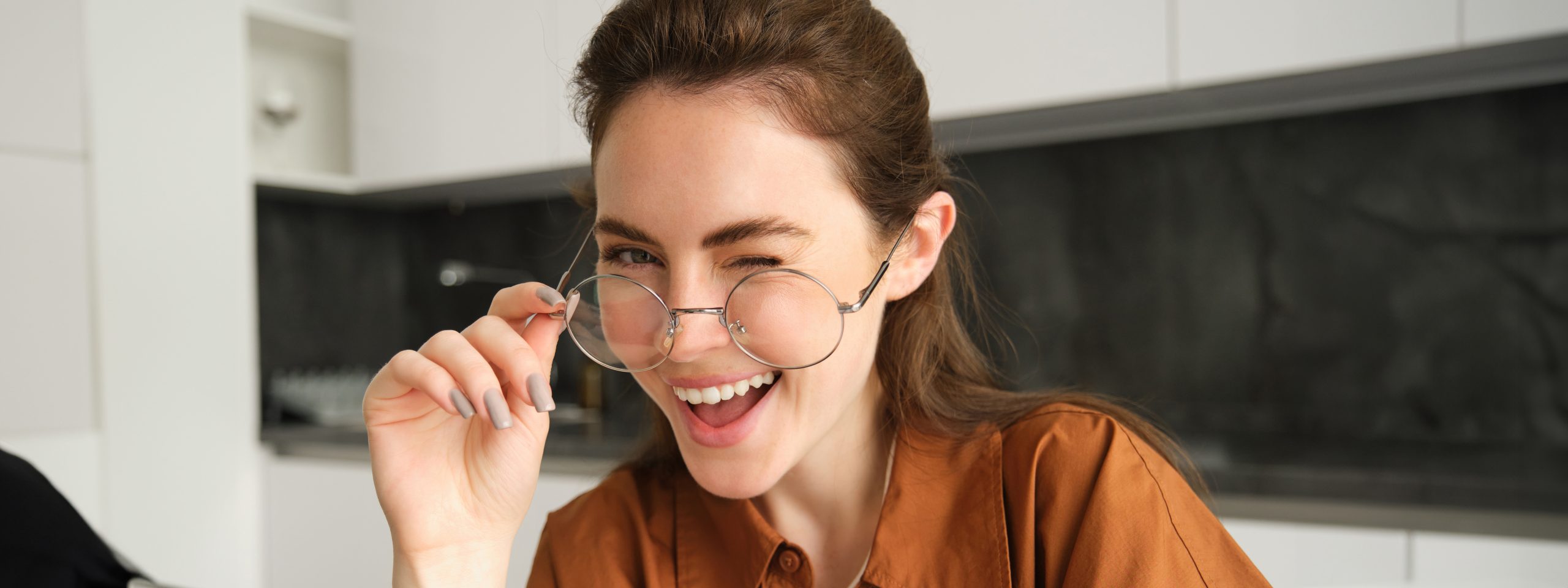 Portrait of beautiful young woman, smiling and looking happy, takes-off her glasses and looking at camera, sitting in kitchen at home Portrait of beautiful young woman, smiling and looking happy, takes-off her glasses and looking at camera, sitting in kitchen at home.